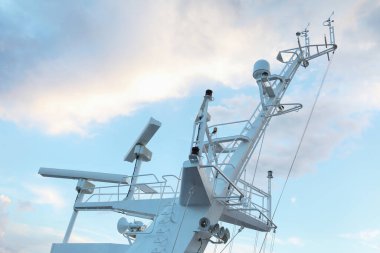 Ship structures, masts, antennas, funnel, ship wheelhouse against the blue sky and clouds. Vessel traveling at ocean.