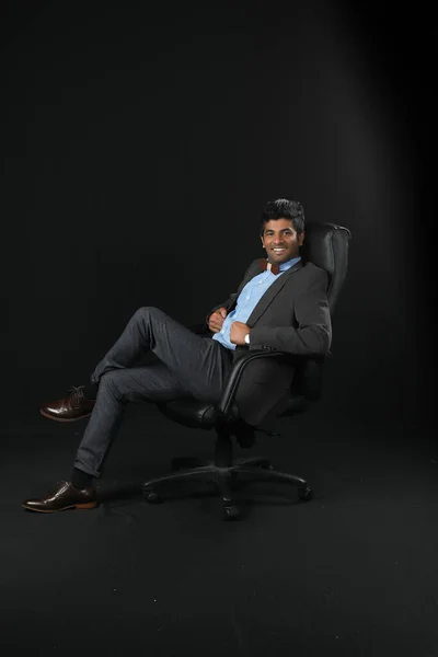 Portrait Young Businessman Sitting Chair Looking Camera Isolated Black Background — Zdjęcie stockowe