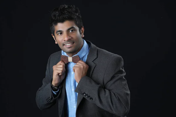 Close up portrait - Indian man ties a bowtie at the collar, correcting wood bow on his grey background