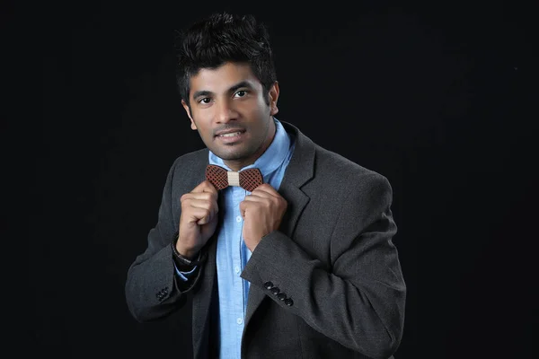 Close up portrait - Indian man ties a bowtie at the collar, correcting wood bow on his grey background