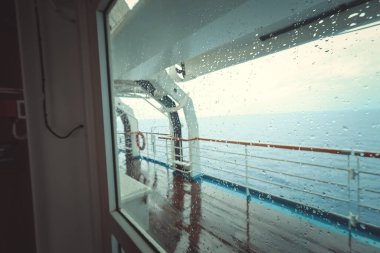 Cruise ship Open deck with Rescue Lifeboats and life buoy through the Window in raindrops