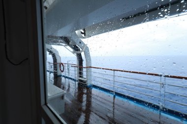 Cruise ship Open deck with Rescue Lifeboats and life buoy through the Window in raindrops