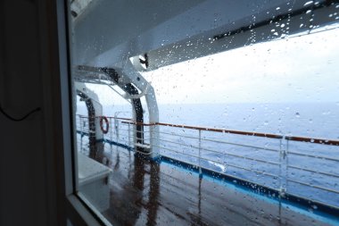 Cruise ship Open deck with Rescue Lifeboats and life buoy through the Window in raindrops