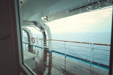 Cruise ship Open deck with Rescue Lifeboats and life buoy through the Window in raindrops