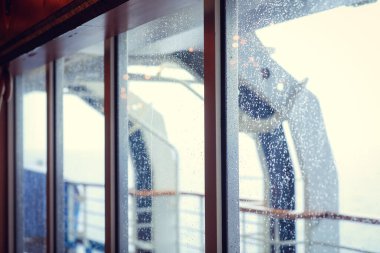 Cruise ship Open deck with Rescue Lifeboats and life buoy through the Window in raindrops