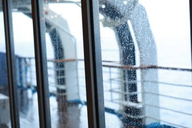 Cruise ship Open deck with Rescue Lifeboats and life buoy through the Window in raindrops