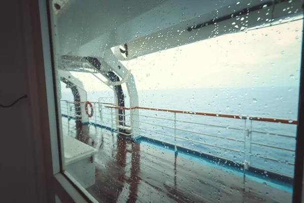 Cruise ship Open deck with Rescue Lifeboats and life buoy through the Window in raindrops
