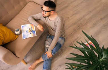 Sakallı ve gözlüklü bir adam koltuğun yanında yere oturur ve evde bir bitki, uçakla bir çizime bakar, üzülür ve bir salgın sırasında uçmayı hayal eder. Gerçek duygular