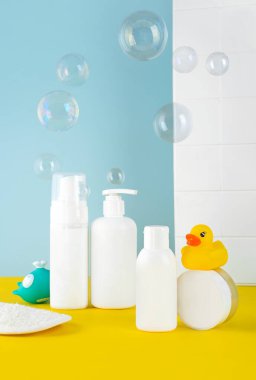 Bebek için banyo aksesuarları banyoda, yakın plan. Şişeler, havlu, balina ve ördek oyuncağı ve mavi sarı arka planda sabun köpükleri olan bir bez. Doğal Hipoalerjenik Kozmetik.