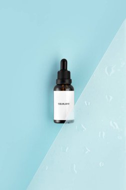 Yaşlanma karşıtı squalane. Kolajeni olan serum ve gölgeli mavi yüzeyde peptid. Hyaluronik asit yağ modeli. Serum kozmetik. Cam şişede damlatıcıyla şeffaf sıvı ürün.