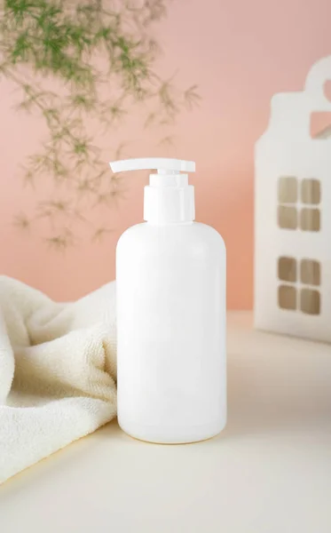 Φυσικό Υποαλλεργικό Αφρόλουτρο για παιδιά. Λευκό πλαστικό μπουκάλι αντλία. Παιδικά καλλυντικά. Μπουκάλια σε ροζ φόντο και μια μαλακή πετσέτα. Παιδικό σπίτι και πράσινο φυτό στο παρασκήνιο — Φωτογραφία Αρχείου