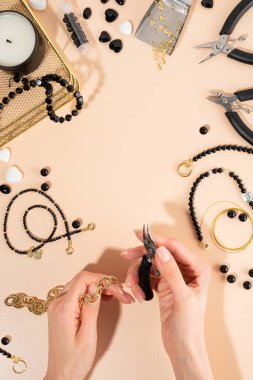 İş yerindeki DIY mücevherleri için aletler ve aksesuarlar. Tel kesicili kadın eli. Bej arka planda düz yatıyordu. Yaratıcı düz yatak, dikey kompozisyon, üst görünüm. El işi hobisi, ev yapımı iş.