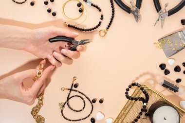 İş yerindeki DIY mücevherleri için aletler ve aksesuarlar. Kablo kesicili bir kadın el. Bej arka planda düz yatıyordu. Yaratıcı düz döşeme, kompozisyon, kopyalama alanı, üst görünüm. Ev yapımı işler, hediyeler yapmak.