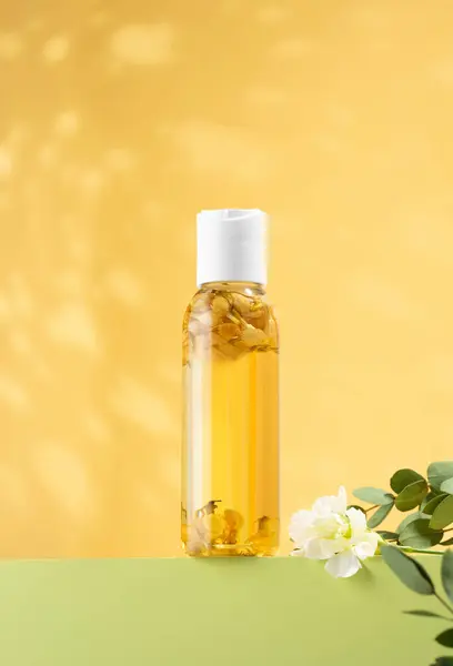 Fresh jasmine flowers inside a bottle of jasmine essential oil standing on a light green podium. Cosmetic oil for body baths on an yellow background. Phytotherapy, aromatherapy, antistress, self-care.