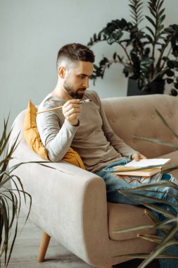 Sanatçı kanepede oturuyor ve elinde bir eskiz defteri tutuyor. Resim öğretmeni, öğrencisinin çalışmalarını stüdyoda değerlendirir. Sanatçının atölyesi, öğrenme süreci, yaşam tarzı.