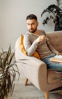 Sanatçı kanepede oturuyor ve elinde bir eskiz defteri ve bir fırça tutuyor. Genç sanatçı stüdyoda ilham arayışında. Sanatçının atölyesi, öğrenme süreci, yaşam tarzı.