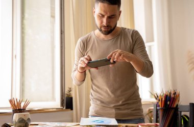 Yaratıcı bir kişi sosyal ağlar için dijital içerik yaratır. Sanatçı stüdyosunda. Genç ressam, eserlerinin fotoğraflarını kurye ile gönderir. DIY konsepti, sanatçı atölyesi.
