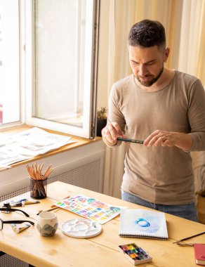 Yaratıcı bir kişi sosyal ağlar için dijital içerik yaratır. Sanatçı atölyesinde. Genç ressam, eserlerinin fotoğraflarını kurye ile gönderir. DIY konsepti, boyama stüdyosu.