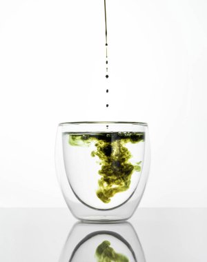 Beyaz gri arka planda klorofil özü olan bir bardak su. Bir bardak suya sıvı klorofil döküyorum. Süper yiyecek kavramı, sağlıklı beslenme, detoks ve diyet. Dikey.