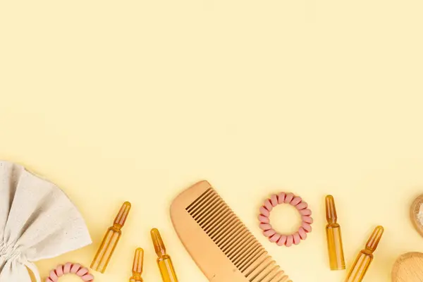 Cosmetic ampoules with serum for hair growth, restoration. Hair comb, Spiral Hair Ties, linen packaging on a yellow paper background. Concept beauty hair, Self-care and wellness. Flat lay. Copy space.
