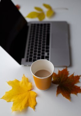 Bir fincan kahve ve sonbahar yapraklarıyla beyaz bir masanın üzerinde duran bir defter. Sonbahar günü.