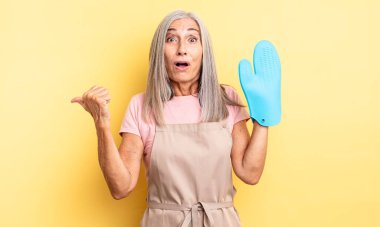 Orta yaşlı, güzel bir kadın inançsızlıktan şaşkın şaşkın bakıyor. fırın eldiveni kavramı