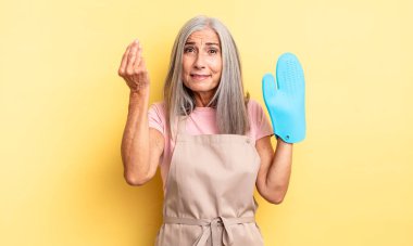 Orta yaşlı, güzel bir kadın kapiş ya da para hareketi yapıp sana ödemeni söylüyor. fırın eldiveni kavramı