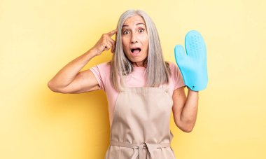 Orta yaşlı, güzel bir kadın şaşırmış görünüyor, yeni bir düşünce, fikir ya da konsept fark ediyor. fırın eldiveni kavramı