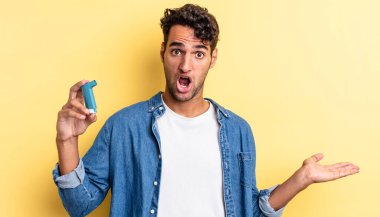 İspanyol yakışıklı adam şaşırmış ve şok olmuş görünüyor. Çenesi düşmüş ve elinde bir nesne var. astım konsepti