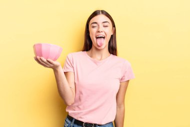 Neşeli ve asi tavırları olan, şaka yapan ve dilini dışarı çıkaran genç İspanyol bir kadın. boş kase kavramı