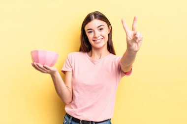 Genç İspanyol kadın gülümsüyor ve arkadaş canlısı görünüyor, iki numarayı gösteriyor. boş kase kavramı