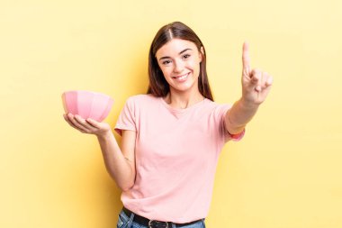 Genç İspanyol kadın gülümsüyor ve arkadaş canlısı görünüyor, bir numarayı gösteriyor. boş kase kavramı