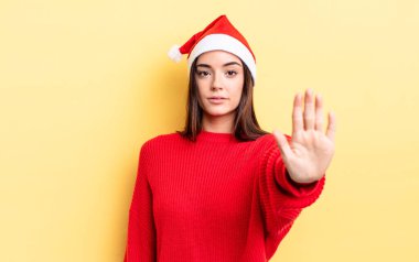 Genç İspanyol kadın ciddi görünüyor. Avuç içini gösteriyor. Durdurma hareketi yapıyor. Chistmas ve yeni yıl konsepti