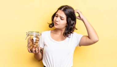 Genç İspanyol kadın mutlu bir şekilde gülümsüyor ve hayal kuruyor ya da şüphe ediyor. kurabiye şişesi konsepti