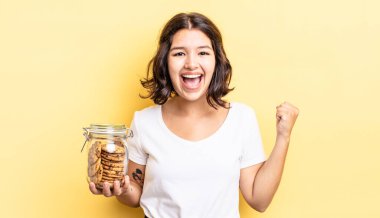 Genç İspanyol kadın şokta, gülüyor ve başarıyı kutluyor. kurabiye şişesi konsepti