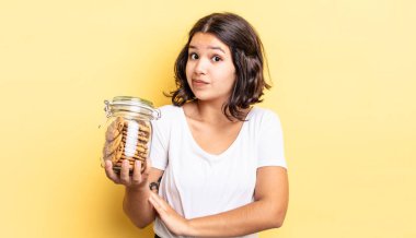 Genç İspanyol kadın omuz silkiyor, kafası karışık ve kararsız. kurabiye şişesi konsepti