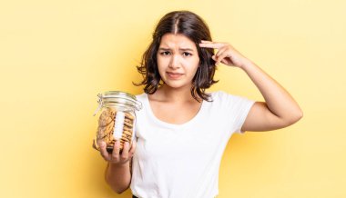 Genç İspanyol kadın şaşkın ve şaşkın hissediyor, senin deli olduğunu gösteriyor. kurabiye şişesi konsepti