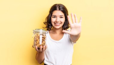 Genç İspanyol kadın gülümsüyor ve arkadaş canlısı görünüyor, beş numarayı gösteriyor. kurabiye şişesi konsepti