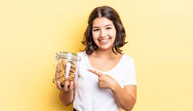 Genç İspanyol kadın neşeyle gülümsüyor, mutlu hissediyor ve bir tarafı işaret ediyor. kurabiye şişesi konsepti