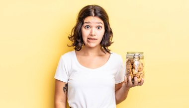 Genç İspanyol kadın şaşkın ve şaşkın görünüyor. kurabiye şişesi konsepti