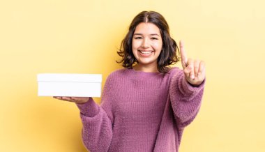 Genç İspanyol kadın gülümsüyor ve arkadaş canlısı görünüyor, bir numarayı gösteriyor. boş kutu kavramı