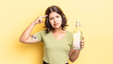 Genç İspanyol kadın şaşkın ve şaşkın hissediyor, senin deli olduğunu gösteriyor. su şişesi kavramı