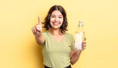 Genç İspanyol kadın gülümsüyor ve arkadaş canlısı görünüyor, bir numarayı gösteriyor. su şişesi kavramı