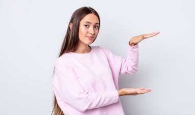 İspanyol asıllı güzel bir kadın bir objeyi iki eliyle fotokopi alanında tutuyor, bir objeyi gösteriyor, sunuyor ya da reklamını yapıyor.