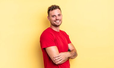 Genç, yakışıklı İspanyol adam kameraya çapraz kollarıyla gülümsüyor ve mutlu, kendinden emin, tatmin olmuş bir yüz ifadesi var.