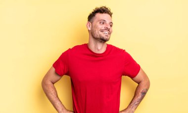 Genç, yakışıklı İspanyol adam mutlu, neşeli ve kendinden emin görünüyor, gururla gülümsüyor ve iki elini de kalçasında istiyor.