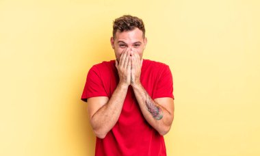 Genç yakışıklı İspanyol adam mutlu, neşeli, şanslı ve şaşkın görünüyor iki eliyle ağzını kapatıyor.