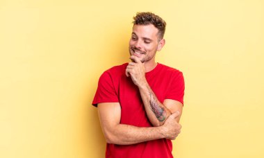 Genç, yakışıklı İspanyol bir adam mutlu, kendinden emin bir ifadeyle gülümsüyor. Elleri çenesinde, merak ediyor ve yan tarafa bakıyor.