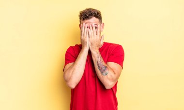 Genç, yakışıklı İspanyol adam elleriyle yüzünü kapatıyor, parmaklarının arasından şaşkın bir ifadeyle yan tarafa bakıyor.
