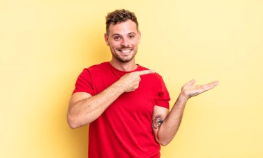 Genç, yakışıklı İspanyol adam gülümsüyor, mutlu, kaygısız ve tatmin olmuş hissediyor, fotokopi alanındaki konsepte ya da fikre işaret ediyor.